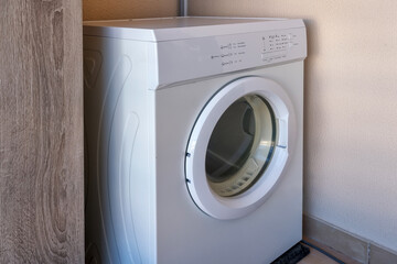 A compact washing machine sits against a wall in a tidy laundry space, showcasing its simple design...