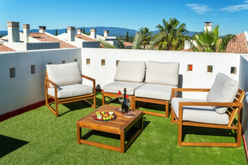 A cozy terrace offers plush seating and a wooden table filled with snacks, surrounded by a blue sky and distant mountains for a peaceful getaway