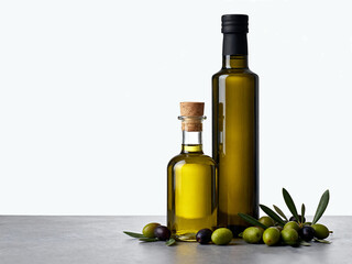 Olive oil bottles with olives and leaves on a gray surface against a white background