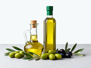 Olive oil in glass bottles with green and black olives and leaves on a light surface