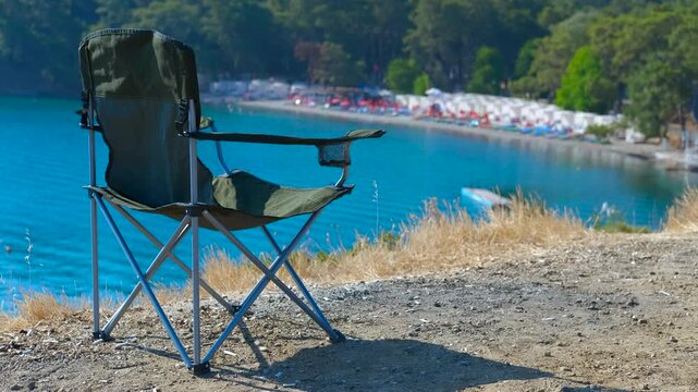Freedom and privacy on holiday. Empty folding chair overlooks a bustling beach filled with vibrant umbrellas. The scene captures a moment of solitude against the lively backdrop of summer vacationers