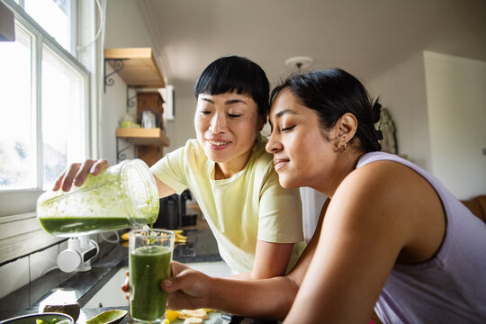 Adult mother and teen daughter happily making green smoothie in home kitchen - Powered by Adobe