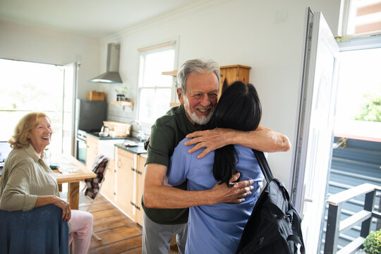 Senior man hugs adult caregiver happily at home kitchen