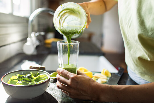 Focused adult pouring green smoothie in home kitchen