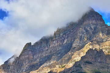 Majestic Rocky Mountain Peak with Dramatic Cloud Cover and Sunlit Cliff Faces