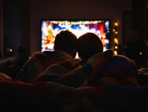 Two children snuggled under a colorful blanket watching a festive movie on TV - Powered by Adobe