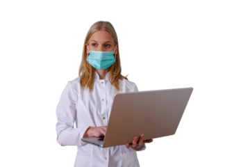 Female healthcare professional wearing face mask and lab coat, holding and typing on laptop, working with medical technology