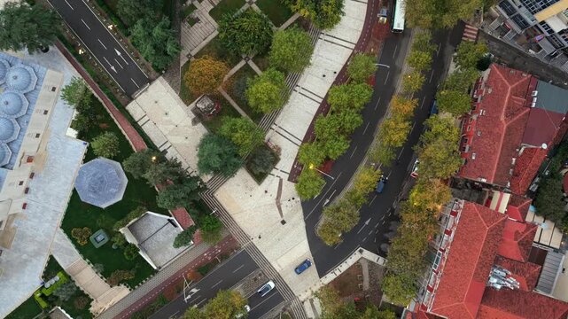 Aerial top-down video of Tirana, Albania, Elbasani road, autumn trees, and surrounding urban architecture.