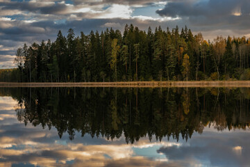 Colourful autumn landscape in the forest next to a lake during sunset, water reflections and colourful sky