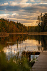 Colourful autumn landscape in the forest next to a lake during sunset, water reflections and colourful sky