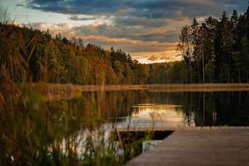 Colourful autumn landscape in the forest next to a lake during sunset, water reflections and colourful sky