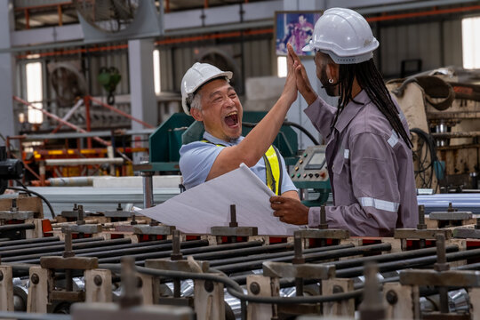 Technician industrial worker with blueprint inspecting aluminum metal sheet machine check stock materials in steel coil storage area, rolls metal sheet high quality durable meet standards industry.