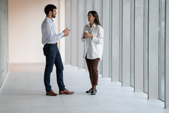 Business colleagues having coffee break conversation in office hallway