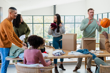 Diverse volunteers sorting and folding clothes at table in community center with donation boxes