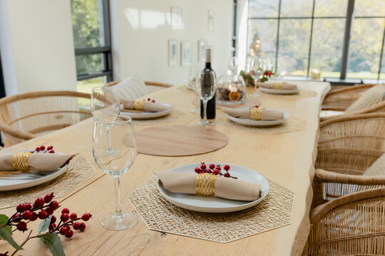 Fototapeta Rustic wood dining table featuring woven placemats, plates and wine glasses in light from window