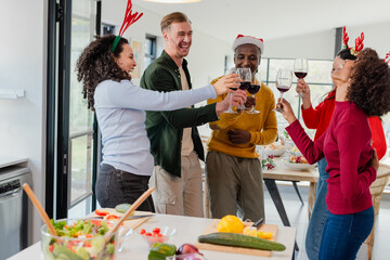 Diverse friends wearing headbands toasting wine glasses while preparing salad on kitchen countertop