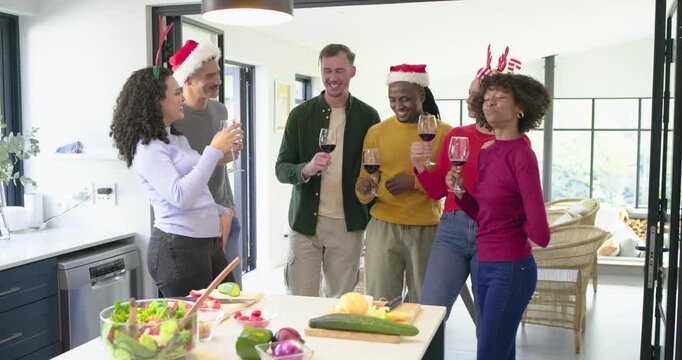 Diverse friends wearing holiday hats after toasting wine, slicing cucumber tossing salad at island