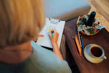 Woman drawing work-life balance wheel sitting on the sofa at home. Self-reflection and life...