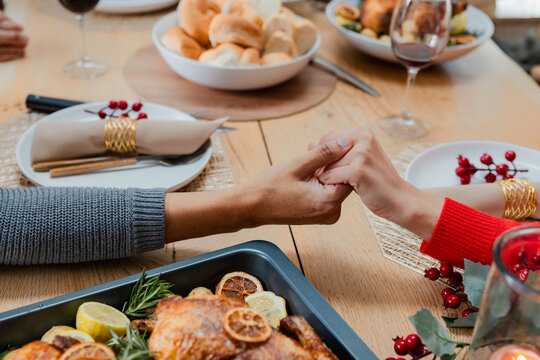 Diverse couple holding hands across wooden dining table with roasting pan and wine glasses at home