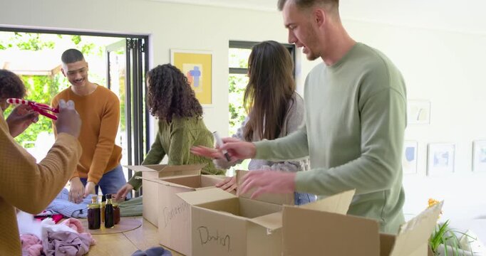 Diverse volunteers sorting and packing donation boxes as they passing basketball at dining table - Powered by Adobe