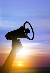 Silhouette hand holding megaphone at sunrise, voice of change and announcement concept