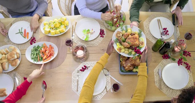 Diverse family starting dinner, serving roast chicken platter and salad with tongs at dining table