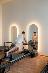 Man training pilates on the reformer bed. Reformer pilates studio machine for fitness workouts in gym. Fit, healthy and strong authentical body. Fitness concept