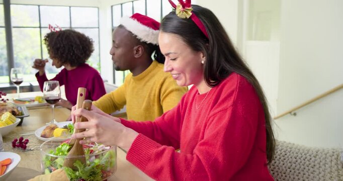 Diverse group gathering for holiday meal at table tossing salad, carving turkey, raising glasses
