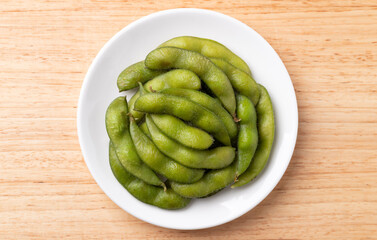 Boiled Edamame beans (Japanese soybeans) on white plate, Table top view