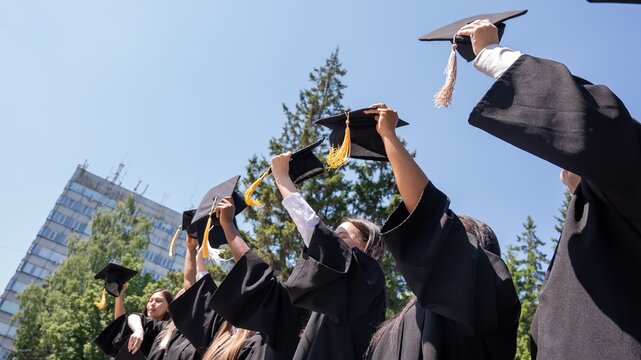 Young women of different nationalities pull graduation caps up.