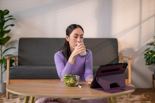 Woman relaxing at home, drinking milk, eating salad, using tablet