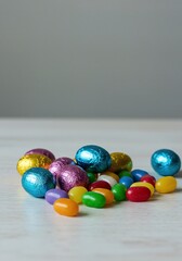 Pastel foil wrapped chocolate eggs and colorful jelly beans spilled onto a tabletop, symbolizing the sweetness of spring holidays ,assortment ,food ,wrapper
