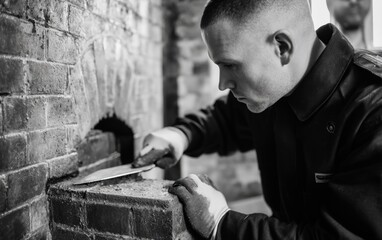 Fototapeta premium Black and white portrait of a technician in a navy uniform and gloves meticulously working on a brick structure, brick oven, close-up shot