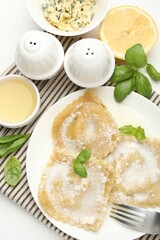 Delicious ravioli with cream sauce and basil served on white table, flat lay
