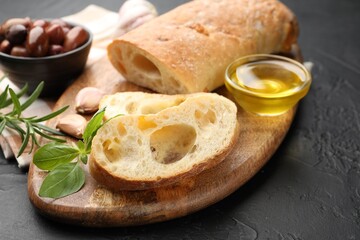 Fresh cut ciabatta, oil, olives, garlic, rosemary and basil on dark textured table, closeup