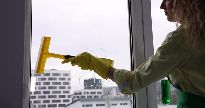 Woman cleaning window with squeegee and detergent indoors, closeup
