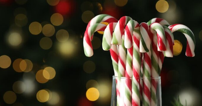 Many candy canes in glass against blurred background with twinkling Christmas lights, closeup. Bokeh effect