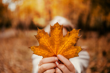 Blonde woman holding a vibrant maple leaf in a beautiful autumn forest