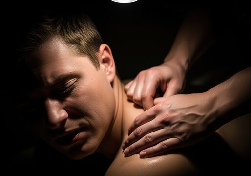 Intense close up of man grimacing while receiving deep tissue shoulder massage.