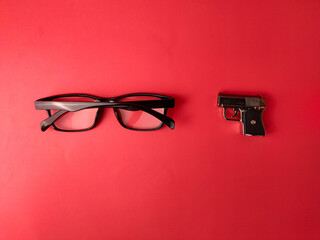 The image displays a pair of black eyeglasses next to a small handgun on a red background