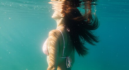 Woman is gazing upwards in clear turquoise water, sunlight dappling her skin gently.