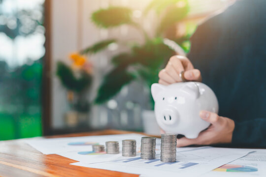 Person saving money with a piggy bank and stacked coins on financial documents, symbolizing budgeting, investment planning, personal finance growth, and effective money management for future financial