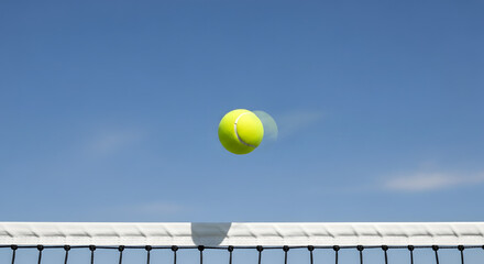 Tennis ball in motion over a net against a bright blue sky