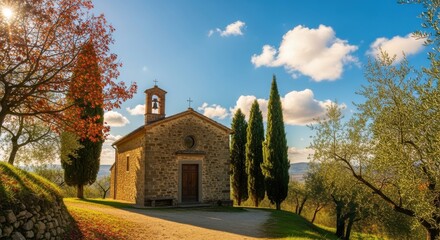 Picturesque tuscan chapel bathed in sunlight among autumnal foliage under a vibrant blue sky