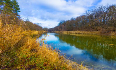 calm river with forest on coast under blue cloudy sky, beautiful autumn seasonal outdoor scene