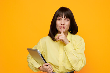 Silhouette of a thoughtful woman in a pale yellow shirt holds a clipboard and gestures for silence against a bright orange backdrop, conveying focus, secrecy, and creative planning.