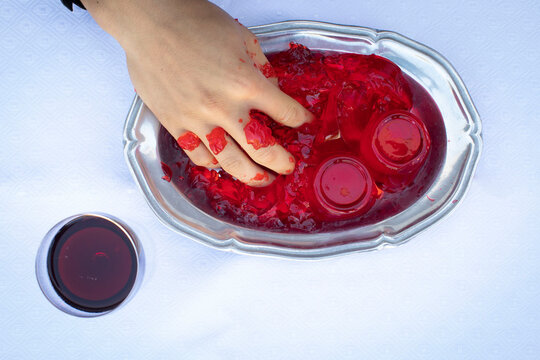 Hand grabbing red jello cubes from a silver platter on a white tablecloth