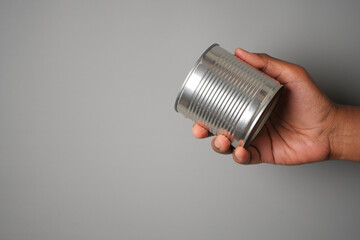 Shiny metal can in hand on gray background