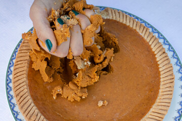Person's hand in a pumpkin pie, smashing it
