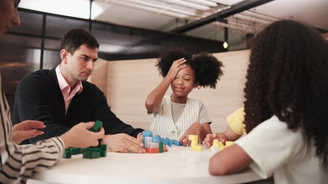 Group of multiracial students and teachers playing fun mathematical puzzle game on tables together, creatively learning in primary class, kids challenge for wisdom at elementary international school.